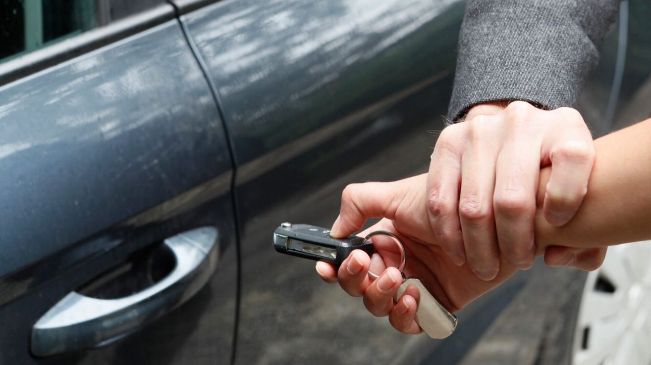 A person is holding a key in their hand, possibly preparing to unlock a car. The key is on a silver keyring.