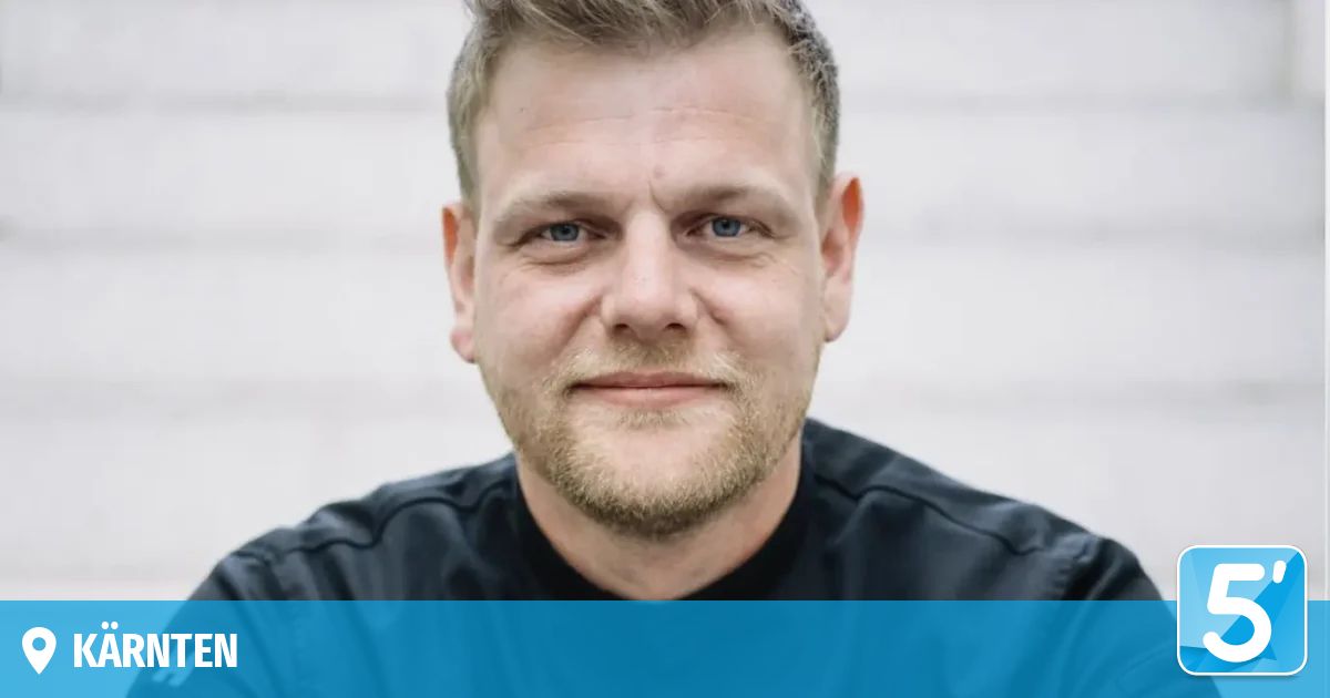 Ein Mann mit kurzen blonden Haaren und Bart lächelt für ein Foto. Er trägt ein schwarzes Shirt.