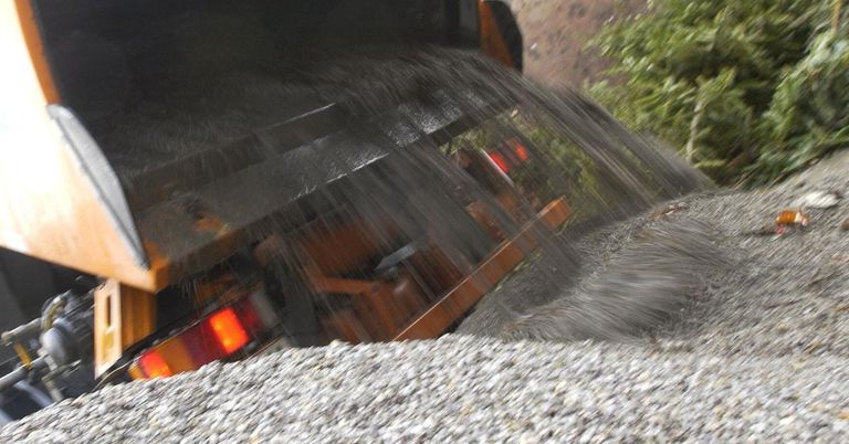 Ein Baufahrzeug kippt Kies aus seinem Fach auf einen Haufen auf dem Boden.