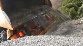 A construction vehicle pours gravel out of its compartment onto a pile on the ground.