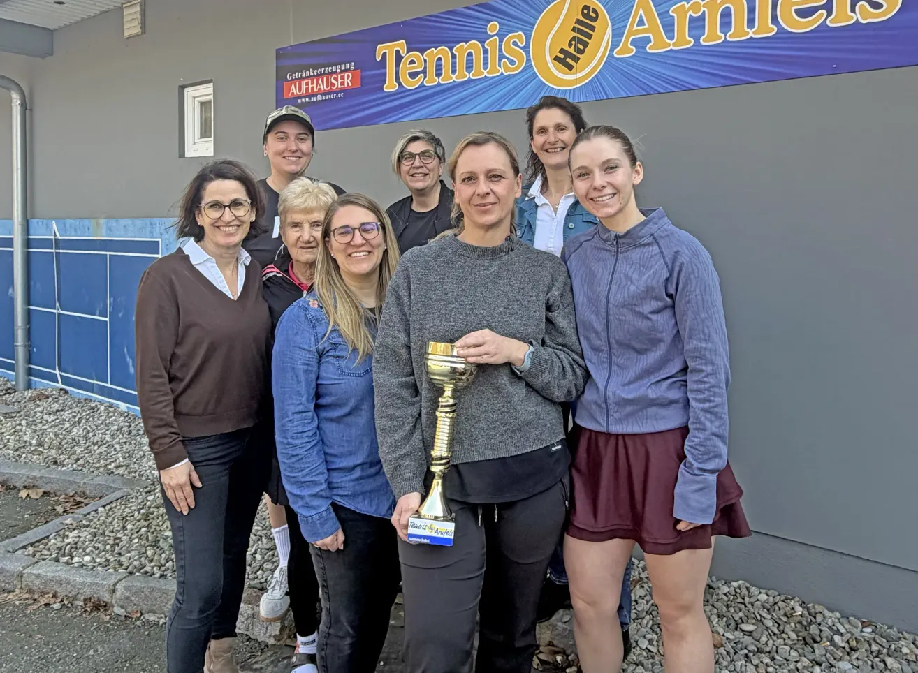 Eine Gruppe von Frauen steht vor einem Gebäude. Eine Frau hält eine goldene Trophäe. Sie alle sehen glücklich aus.