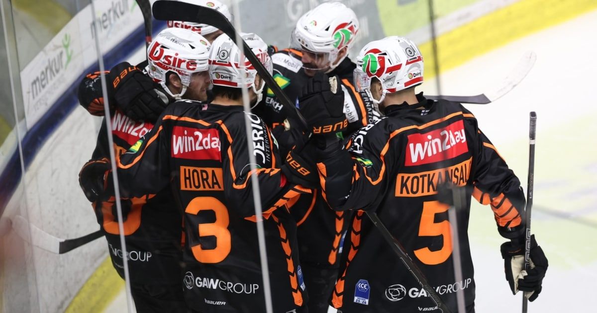 Eine Gruppe von Eishockeyspielern in schwarzen und orangefarbenen Trikots feiert einen Sieg auf einer Eisbahn.