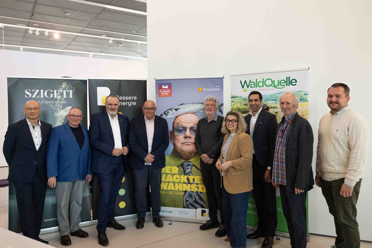 Eine Gruppe von Menschen steht vor einem Banner mit einem Fisch und einem Mann mit Brille. Die Gruppe besteht aus Männern und Frauen in formeller Kleidung. Sie nehmen wahrscheinlich an einer Veranstaltung oder Konferenz teil.