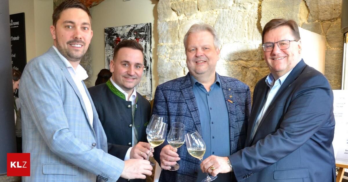 Four men are smiling and posing for a picture while holding wine glasses. They are dressed in suits and are standing next to each other.
