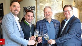 Four men are smiling and posing for a picture while holding wine glasses. They are dressed in suits and are standing next to each other.