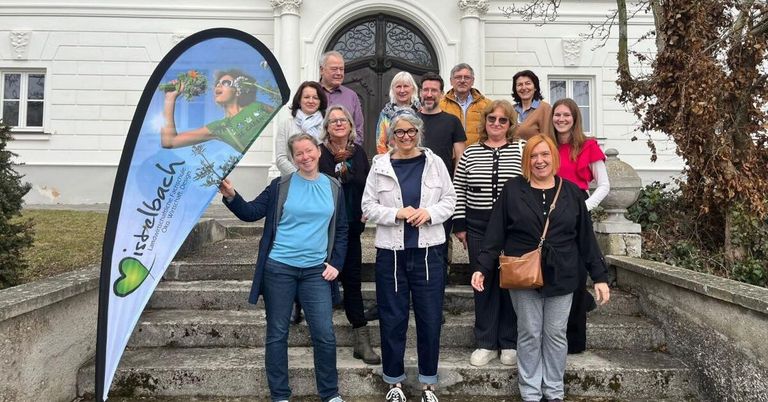 Eine Gruppe Erwachsener posiert für ein Foto vor einem Gebäude, einige halten ein Banner.