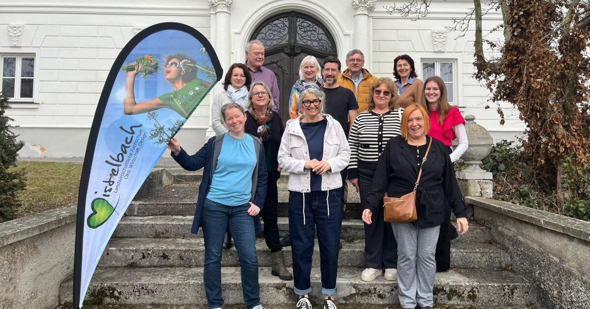 Eine Gruppe Erwachsener posiert für ein Foto vor einem Gebäude, einige halten ein Banner.