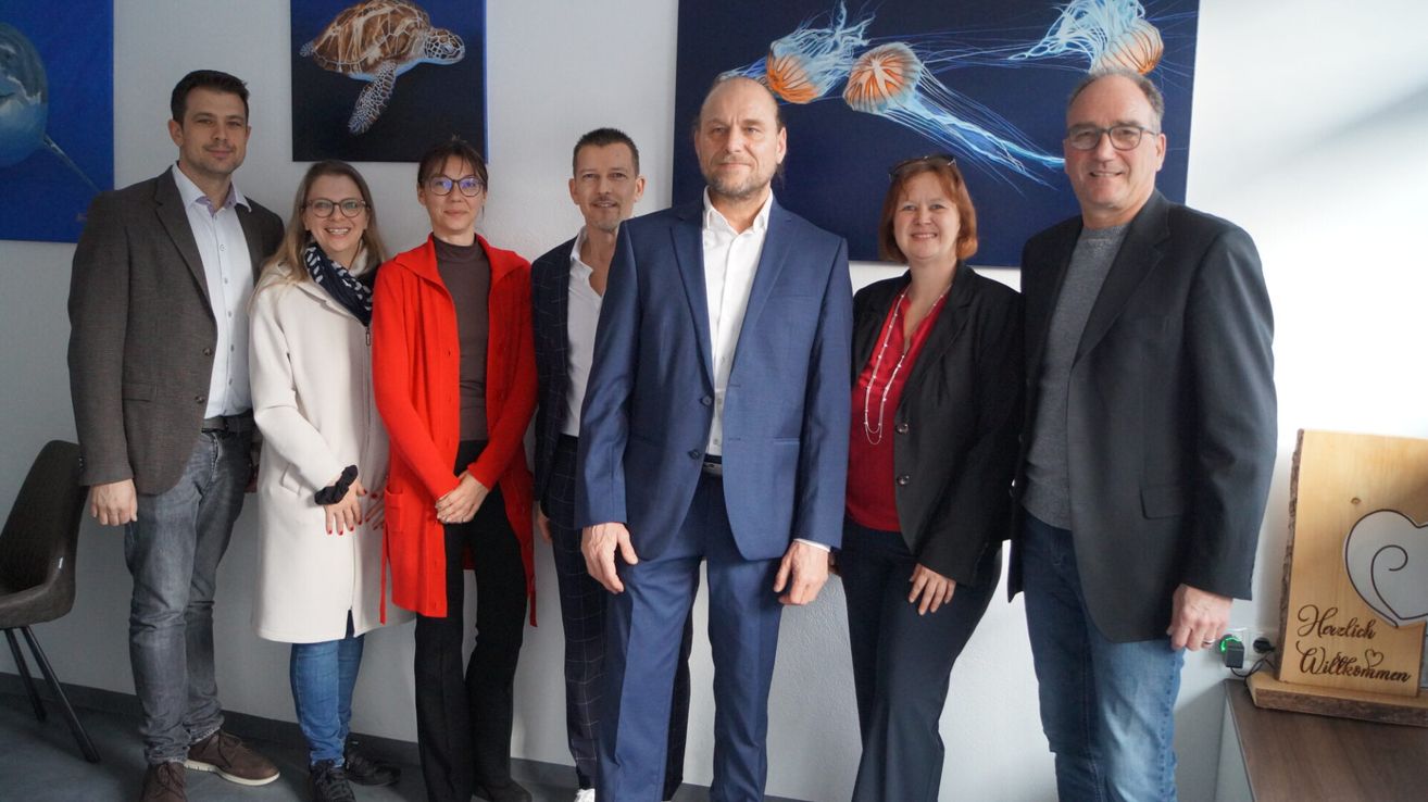 A group of people, five women and two men, stand in front of a wall with two large paintings. They are dressed in winter clothes and appear to be posing for a photograph.