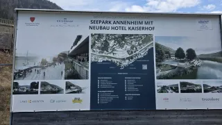 A large informational sign for a project in Seepark Annenheim. It shows a new hotel Kaiserhof. The sign has various sections, including a map, project details, and amenities. It is surrounded by scenic images.