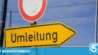 A yellow road sign with black writing 'Umleitung' attached to a red and white circular sign on a pole with wires. The sign indicates a detour.