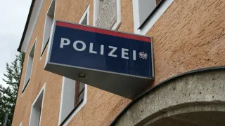 Ein blaues und weißes Schild mit der Aufschrift 'POLIZEI' ist an der Seite eines Gebäudes angebracht. Das Gebäude hat mehrere Fenster und einen gewölbten Eingang.