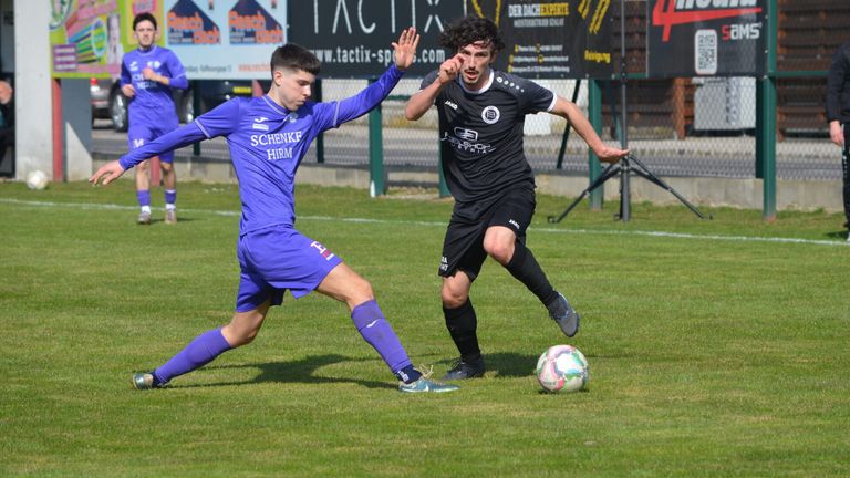 Zwei Fußballspieler sind auf einem Feld. Einer in Lila und einer in Schwarz. Sie versuchen, den Ball zu bekommen.