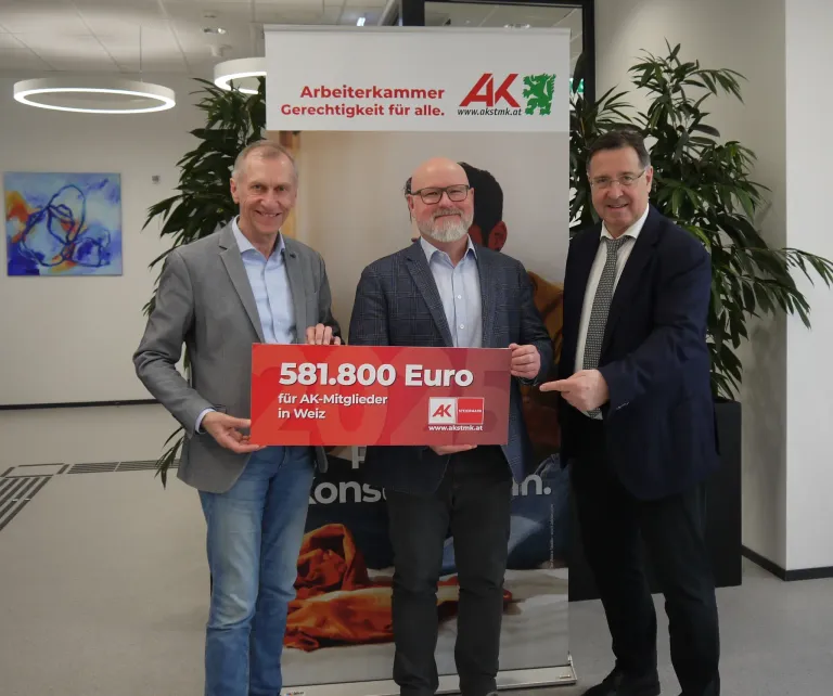 Drei Männer stehen vor einem Plakat und halten ein großes rotes Schild mit der Aufschrift 581.800 Euro für AK-Mitglieder in Weiz.