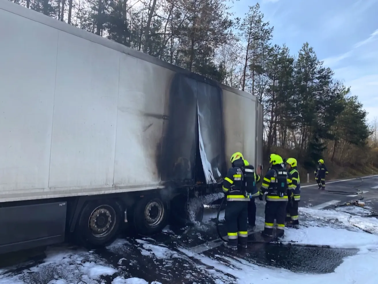 Feuerwehrleute löschen einen Brand an einem Sattelschlepper, indem sie Wasser sprühen, wobei eine Person eine Wasserspritze in der Nähe des brennenden Bereichs hält.