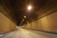 Ein dunkler Tunnel mit gelben Wänden und einer einzelnen Straßenlaterne, die die Straße beleuchtet. Der Tunnel erscheint lang und leer, mit weißen Markierungen auf der Straße.