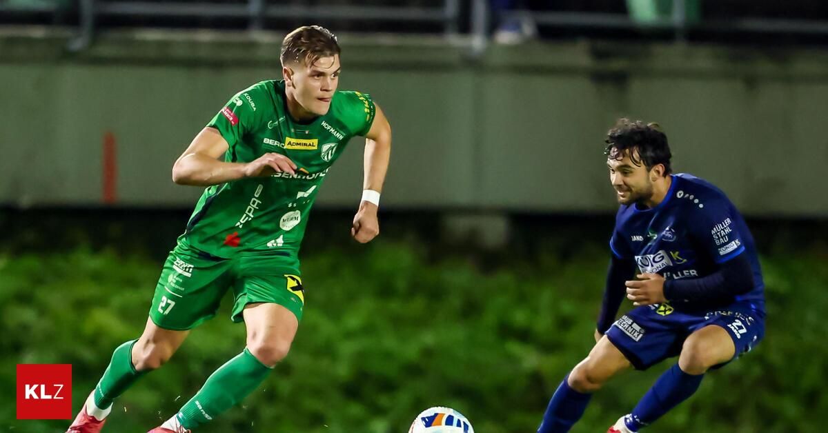 Zwei Fußballspieler in verschiedenen Trikots rennen auf den Ball zu, einer in Grün und der andere in Blau.