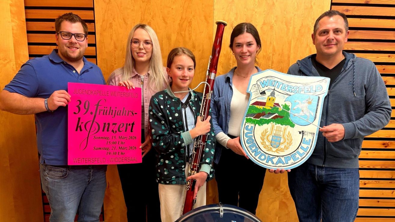 Fünf junge Leute posieren für ein Foto, halten ein Schild und ein Musikinstrument. Das Schild steht 'Frühlingskonzert' und 'Weitersfeld-Wiedersaal'. Das Mädchen in der Mitte hält eine Fagott. Sie lächeln.