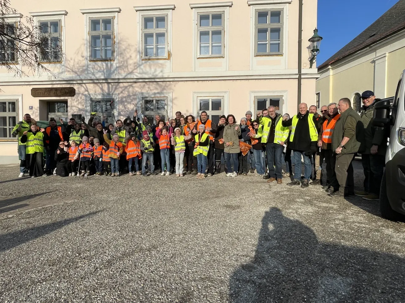 Eine Gruppe von Menschen in orangefarbenen Westen steht vor einem Gebäude. Einige winken.