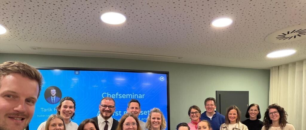 A group of people smiling for a photo during a seminar with a screen behind them showing the word 'Chefseminar'.