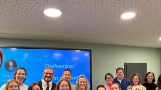 A group of people smiling for a photo during a seminar with a screen behind them showing the word 'Chefseminar'.