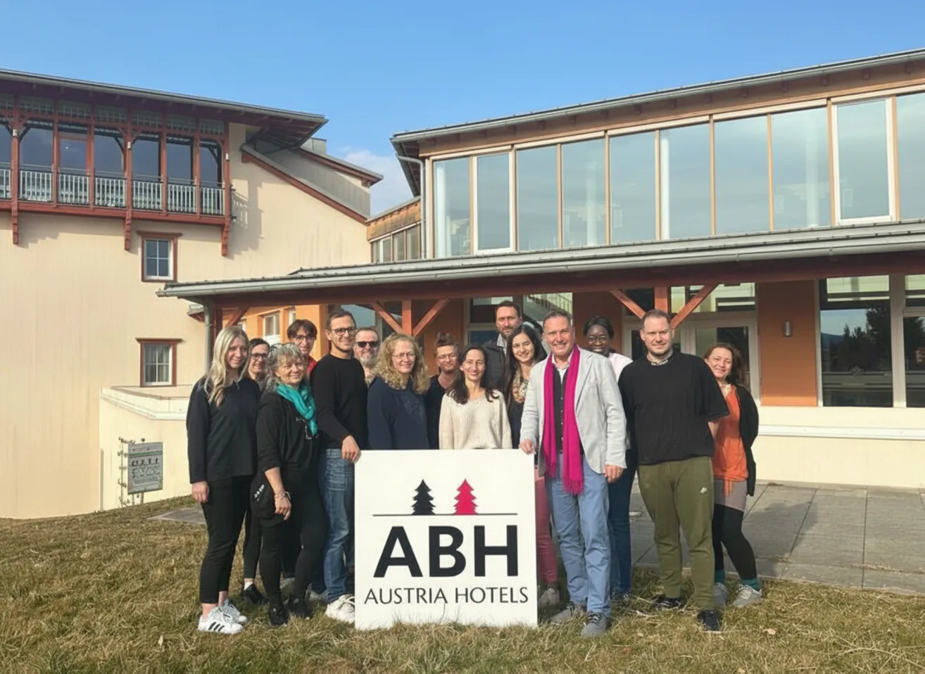 Eine Gruppe von Menschen steht draußen vor einem Gebäude mit dem Schild ABH Austria Hotels. Sie lächeln und posieren für ein Foto.