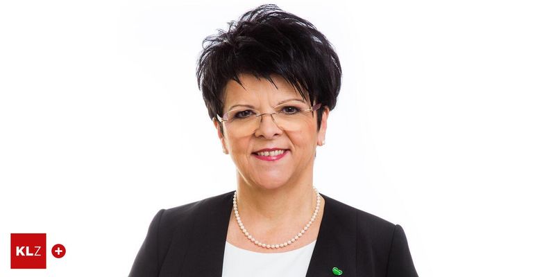 A woman with short black hair, glasses, and a pearl necklace poses for a photograph wearing a white shirt and black blazer.