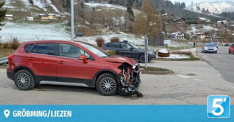Ein roter SUV mit beschädigter Front steht in einem verschneiten Bereich, dahinter ein schwarzer SUV und Häuser im Hintergrund.