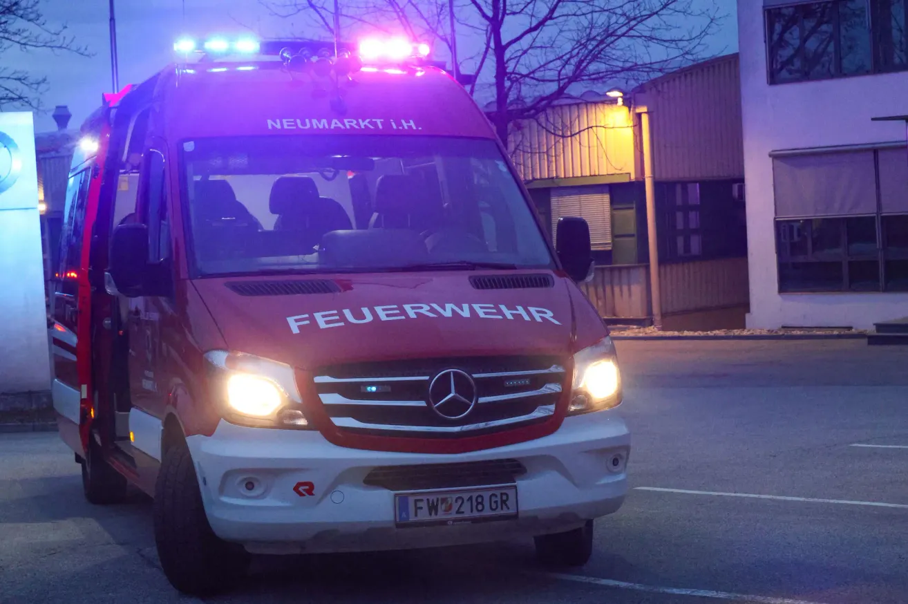 Ein roter Krankenwagen mit der Aufschrift 'FEUERWEHR' auf der Seite ist mit eingeschalteten Lichtern geparkt, möglicherweise als Reaktion auf einen Notfall.