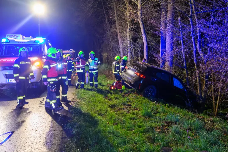 Emergency personnel in helmets and uniforms are attending to a black car that has overturned on the side of the road at night.
