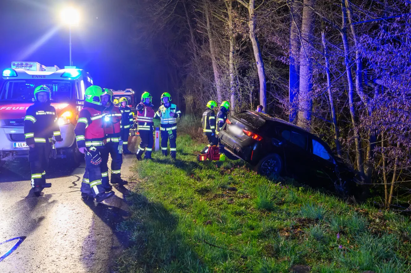 Emergency personnel in helmets and uniforms are attending to a black car that has overturned on the side of the road at night.