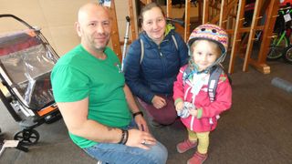 Ein Mann und eine Frau mit einem kleinen Mädchen lächeln für ein Foto, das Mädchen trägt einen Helm und eine rosa Jacke.