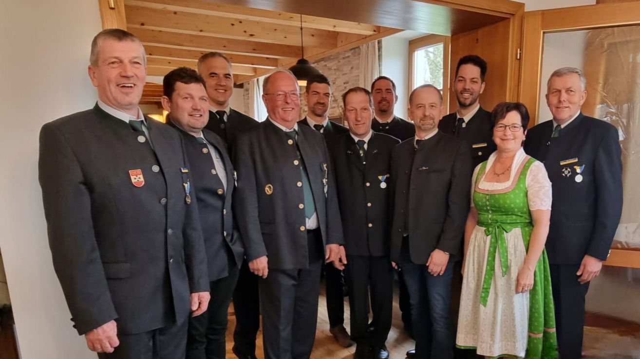 Eine Gruppe von Männern und einer Frau steht drinnen zusammen. Sie tragen alle Uniformen mit Medaillen und Krawatten. Der Raum hat Holzdecken.