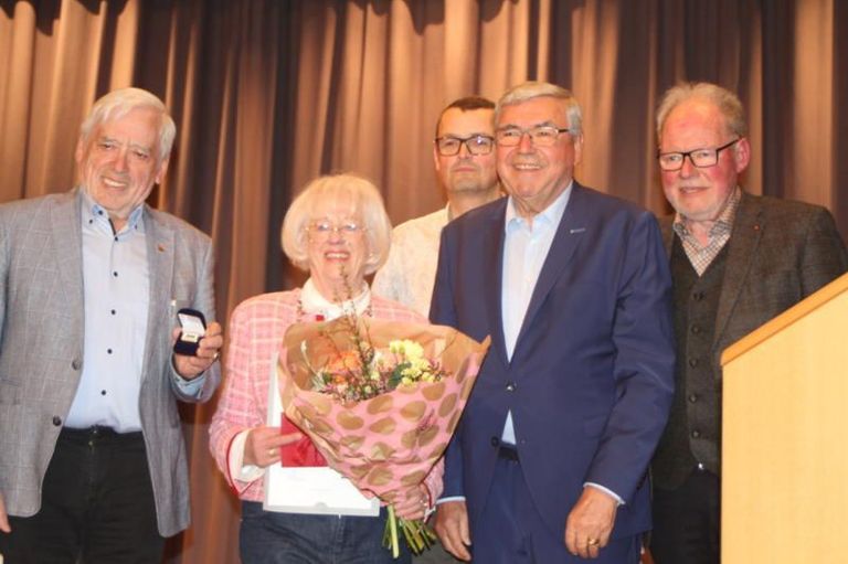 Fünf ältere Personen stehen in einem Raum. Eine Frau hält einen Blumenstrauß. Ein Mann trägt einen Ring am Finger.