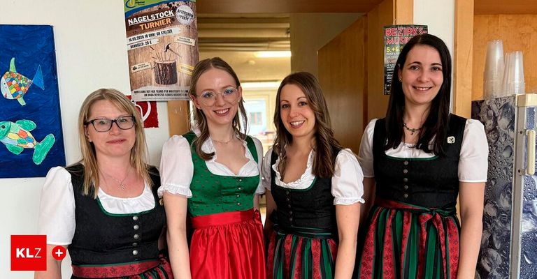 Vier Frauen in traditioneller Kleidung stehen vor einer Tür und lächeln für ein Foto. Ein Plakat an der Wand bewirbt eine Party.