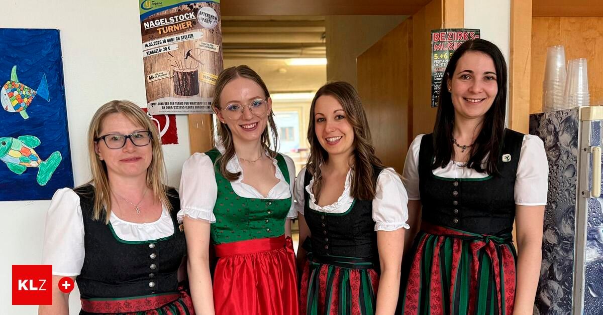 Vier Frauen in traditioneller Kleidung stehen vor einer Tür und lächeln für ein Foto. Ein Plakat an der Wand bewirbt eine Party.