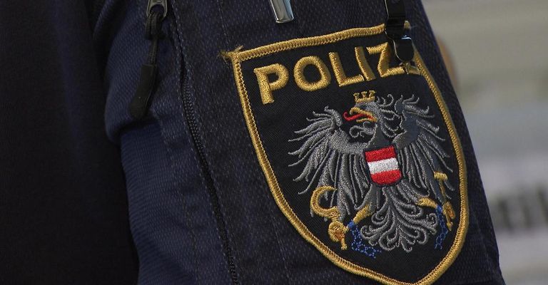 Ein Nahaufnahme eines dunkelblauen Jacken mit gesticktem Polizeiemblem. Das Emblem zeigt einen Adler mit Krone und Schild, und der Schriftzug 'POLIZEI' darüber.