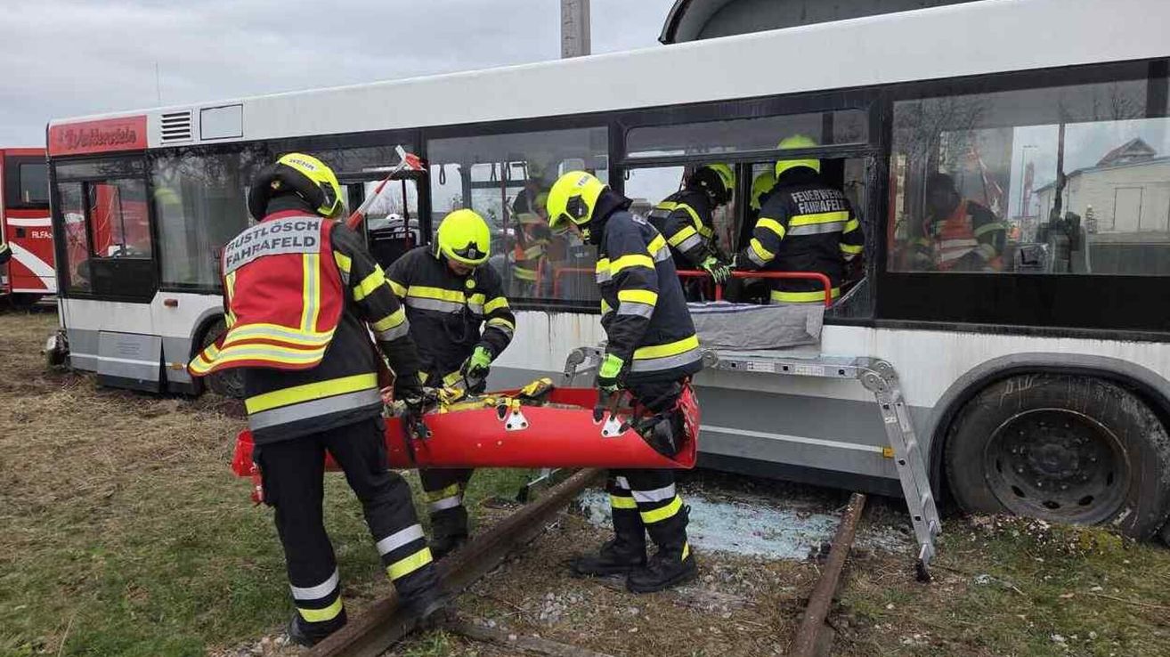 Emergency workers in yellow uniforms are rescuing individuals from a damaged tram on the tracks.