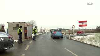 Ein blaues Auto fährt auf einer verschneiten Straße, an der Seite stehen zwei Arbeiter in reflektierenden Westen. Ein rotes Auto ist rechts geparkt.
