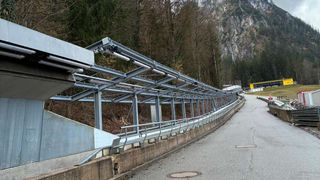 Eine leere Straße mit einer Metallstruktur und Geländern. Im Hintergrund befinden sich Bäume und ein Berg.