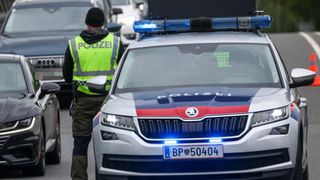 Ein Polizist in einer Warnweste steht neben einem Polizeiauto mit blauer Lampe obenauf.