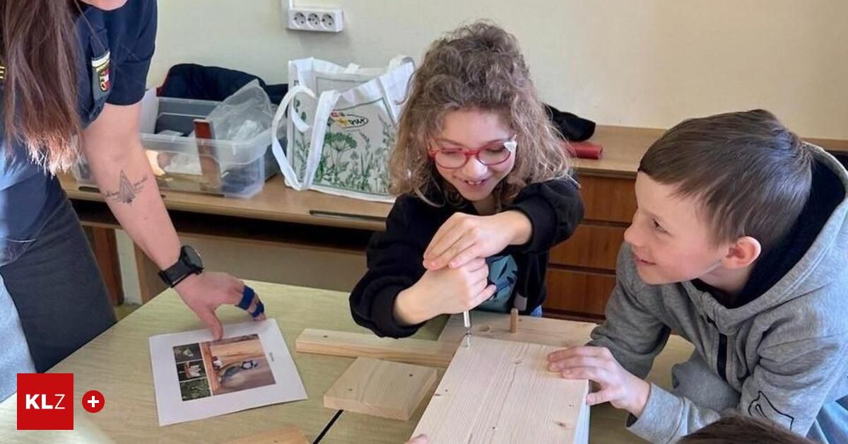 Zwei Kinder arbeiten an einem Holzbastelprojekt mit einem Begleiter in der Nähe, lächelnd, während sie einen kleinen Holzstab bohren.