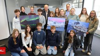 Eine Gruppe junger Menschen und Erwachsener, die für ein Foto posieren, einige halten gerahmte Drucke von Landschaften in der Hand, drinnen.