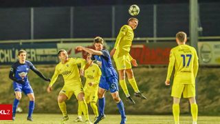 Fußballspieler in gelben und blauen Trikots sind auf dem Feld bei Nacht in Aktion. Ein Spieler in Gelb springt, um den Ball zu köpfen.