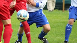 Zwei Fußballspieler, einer in Blau und einer in Rot, kämpfen um einen Ball mit der Aufschrift 'Derby'.