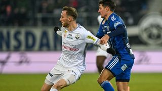 Zwei Fußballspieler sind auf dem Spielfeld in Aktion. Einer ist in Weiß, der andere in Blau, beide kämpfen erbittert.