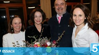 Vier Menschen lächeln und posieren für ein Foto mit Blumen vor ihnen. Sie sind alle formell gekleidet, und der Mann in der Mitte trägt eine rosa Krawatte.