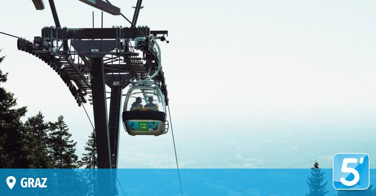 Zwei Personen in einer Seilbahn, möglicherweise einer Gondel, fahren mit Blick auf die Stadt in der Luft.