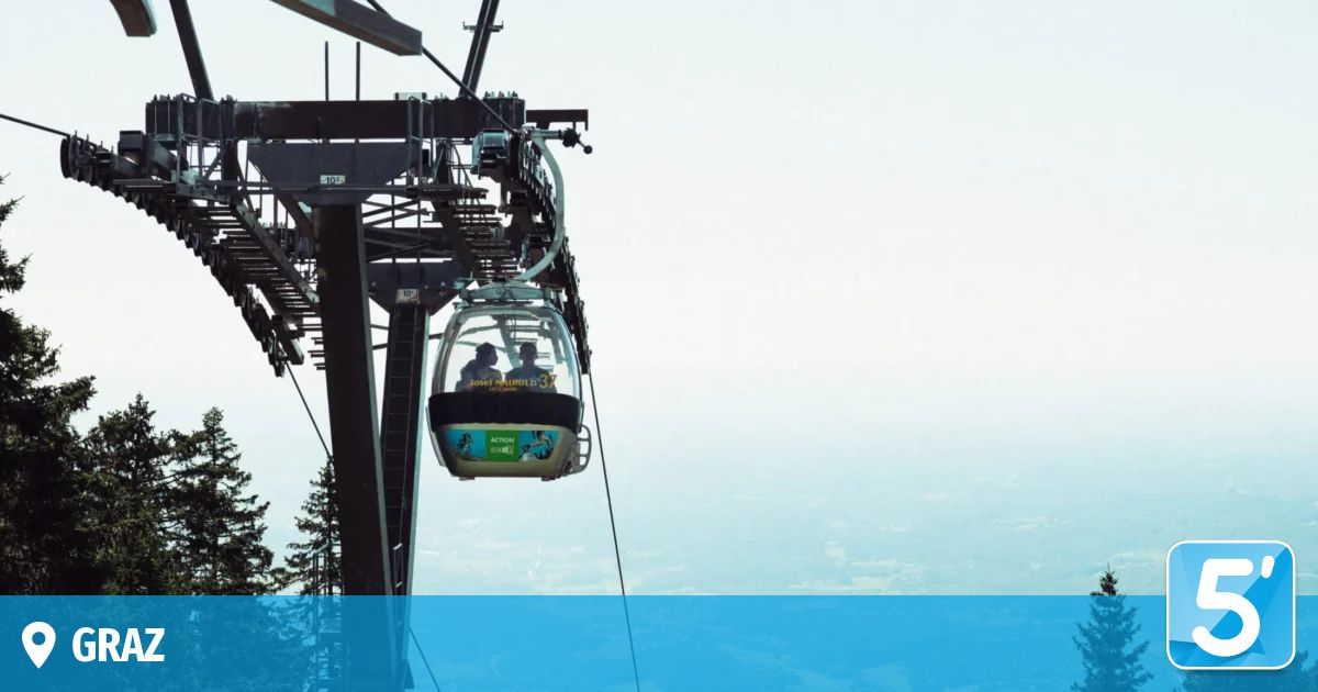 Zwei Personen in einer Seilbahn, möglicherweise einer Gondel, fahren mit Blick auf die Stadt in der Luft.