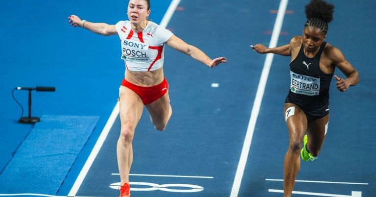 Eine Läuferin in einem weißen und roten Trikot mit Sony läuft auf einer Laufbahn mit einem anderen Läufer in einem schwarzen Trikot.