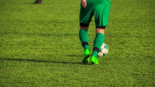 Ein Fußballspieler in grüner Uniform steht auf einem Feld mit einem Fußball in der Nähe.